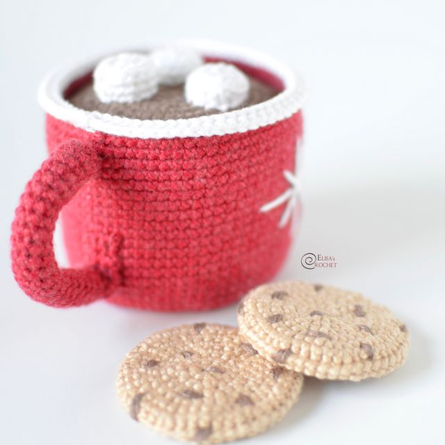 there is a crocheted mug and two cookies on the table