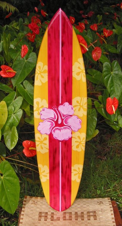 a wooden surfboard sitting on top of a mat in front of some plants and flowers