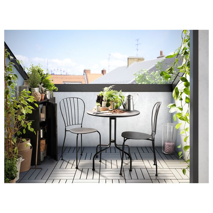 two chairs and a table on a small balcony with potted plants in the corner