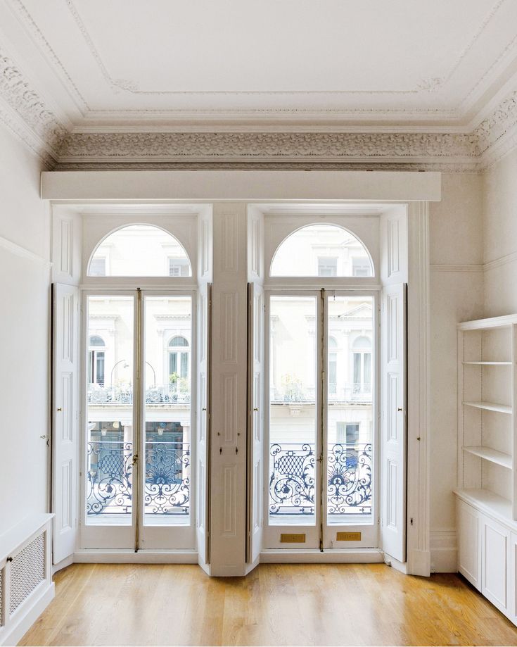 an empty room with two open doors and wooden flooring in front of the windows