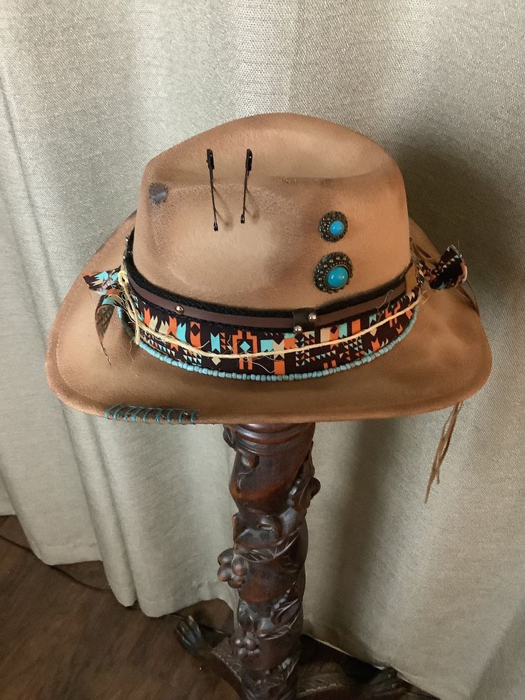 This is a custom weathered hat with incredible detail.  Tan felt with western fabric of orange, turquoise, black and white.  Strand of turquoise beads.  Black and brown hat band with silver studs, silver bull and raw hide ties.  Jute tied around.  Black safety pins.  Turquoise embellishments.  Turquoise stitching on edge.  Adjustable band inside to fit any size. Adjustable Southwestern Felt Hat For Western-themed Events, Rustic Adjustable Felt Hat For Festival, Brown Flat Brim Costume Hat For Festival, Brown Southwestern Hat Bands For Western-themed Events, Southwestern Brown Felt Hat For Rodeo, Southwestern Brown Hat Bands For Rodeo, Southwestern Brown Felt Hat For Western-themed Events, Rustic Festival Hat Bands For Short Brim Hats, Adjustable Western Brown Costume Hats And Headpieces