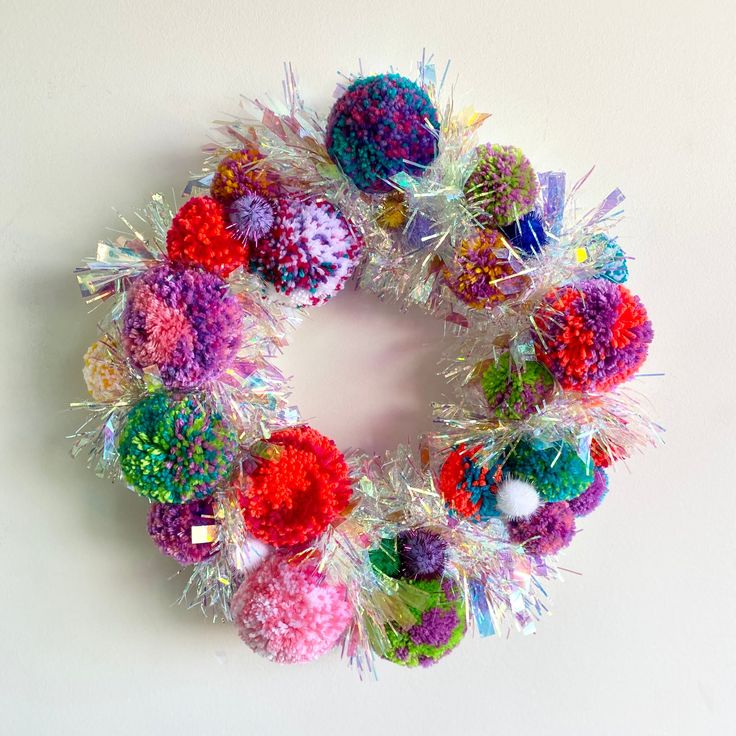 a multicolored christmas wreath with tinsel and pom - poms on it