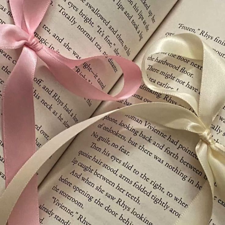 a book with pink ribbon on top of it and an open book in the background