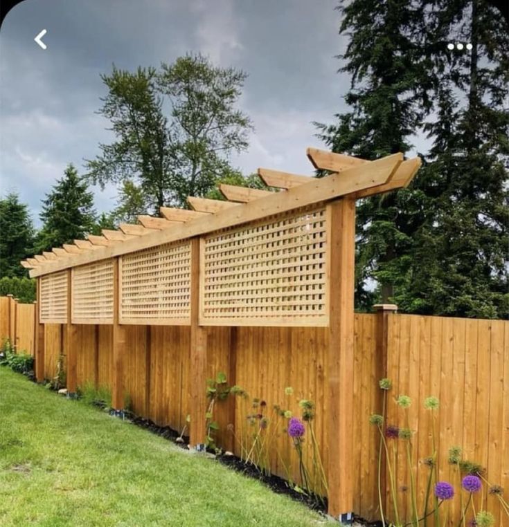 a wooden fence that is next to some grass and flowers on the side of it