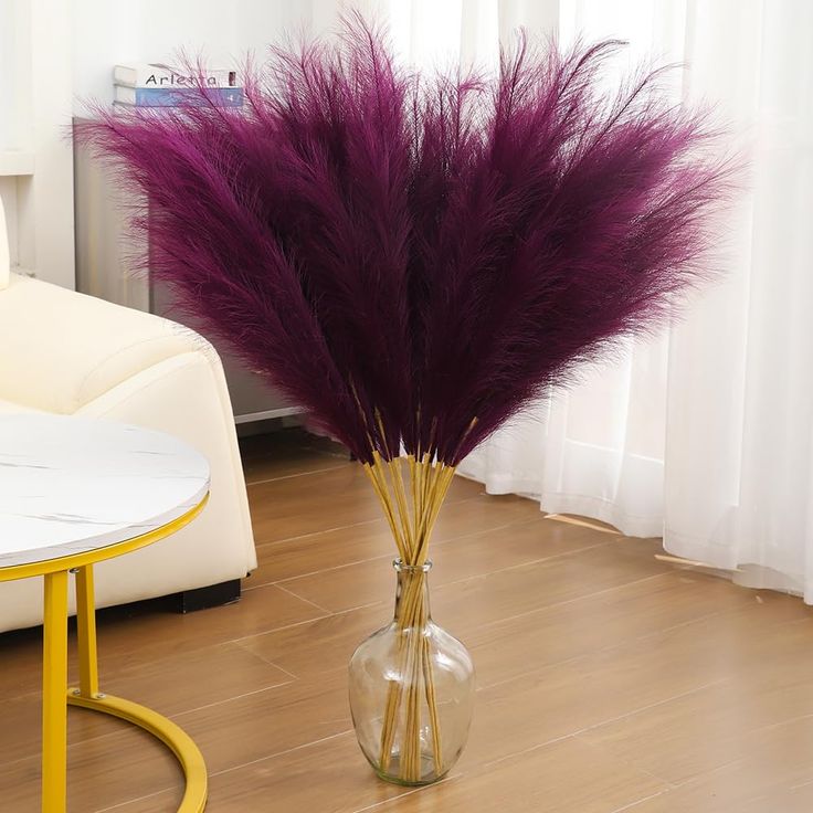 a vase filled with purple feathers sitting on top of a wooden floor next to a white couch