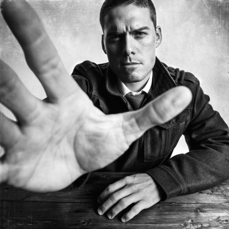 a man sitting at a table holding his hand up to the camera with both hands