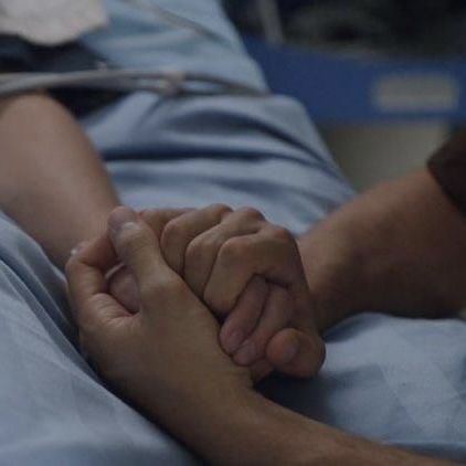 a person laying in a hospital bed holding the hand of another person's arm