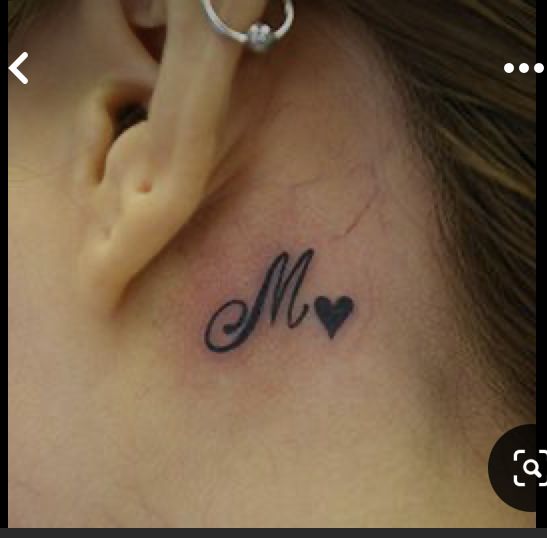 a close up of a person's ear with a heart and m tattoo on it