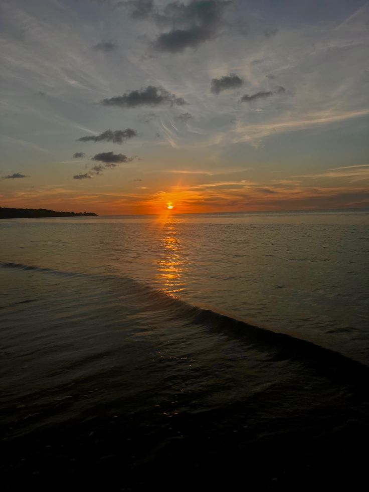 the sun is setting over the ocean with clouds in the sky and water on the beach