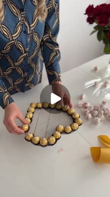 a woman is decorating a heart shaped cake with chocolates and flowers in the background