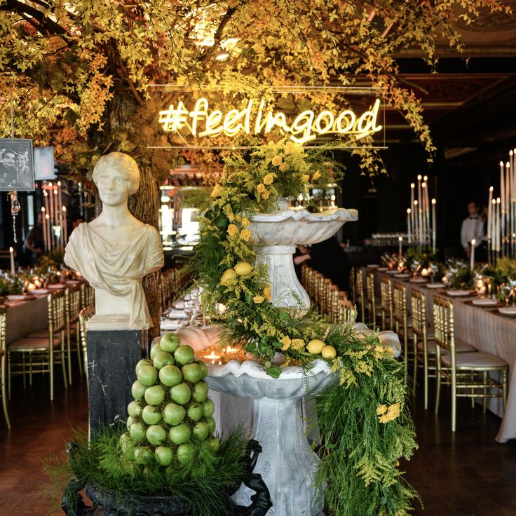 there is a table set up with fruit and greenery in front of a statue