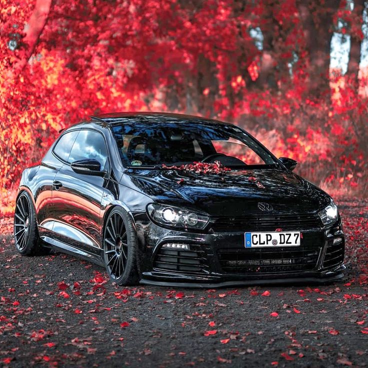 a black car parked on the side of a road in front of trees with red leaves