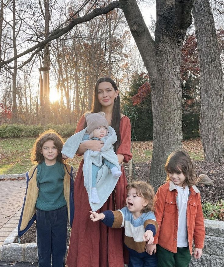 a woman standing next to two children in front of a tree