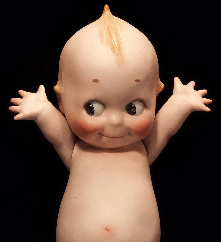 a baby doll with blonde hair and big eyes is posed in front of a black background