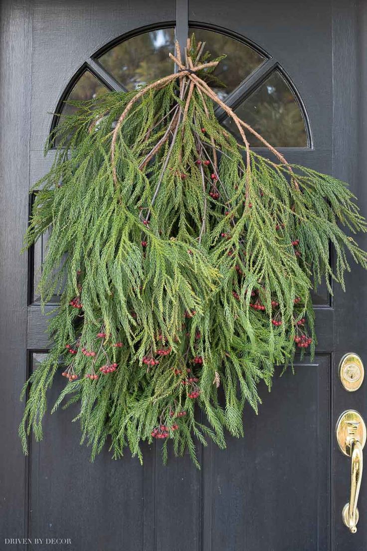 a wreath hanging on the front door of a house with pine needles and berries in it