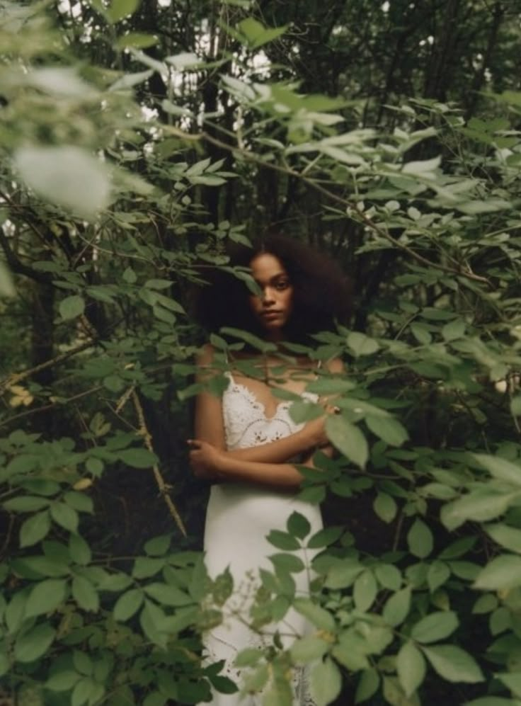 a woman standing in the woods with her arms crossed