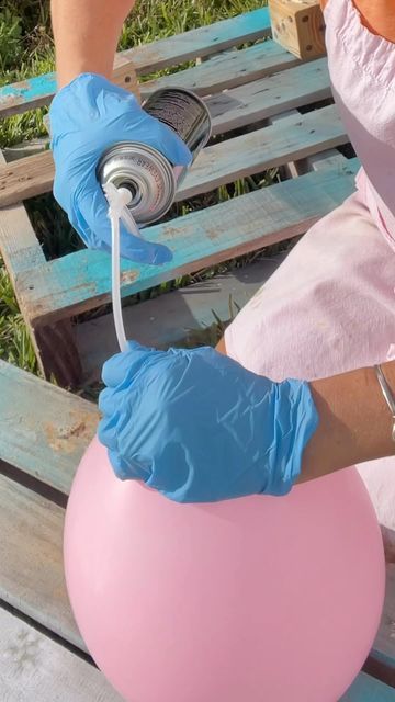 a woman in blue gloves is painting a pink ball with a sprayer on it