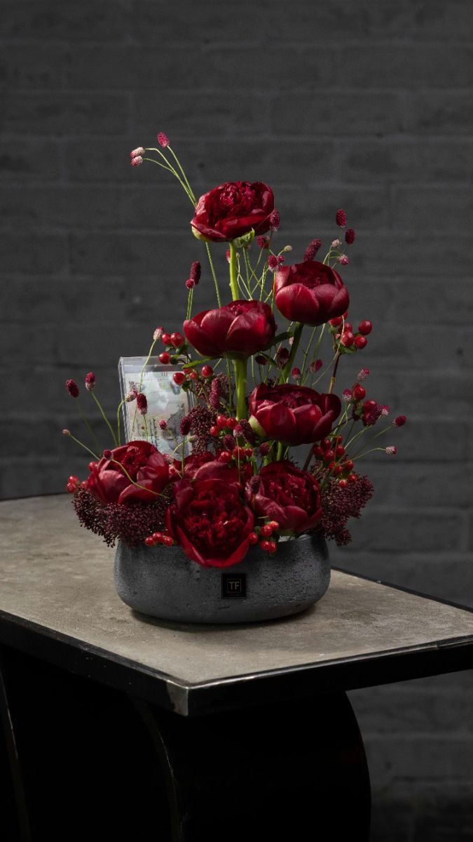 a vase filled with red flowers sitting on top of a table next to a brick wall