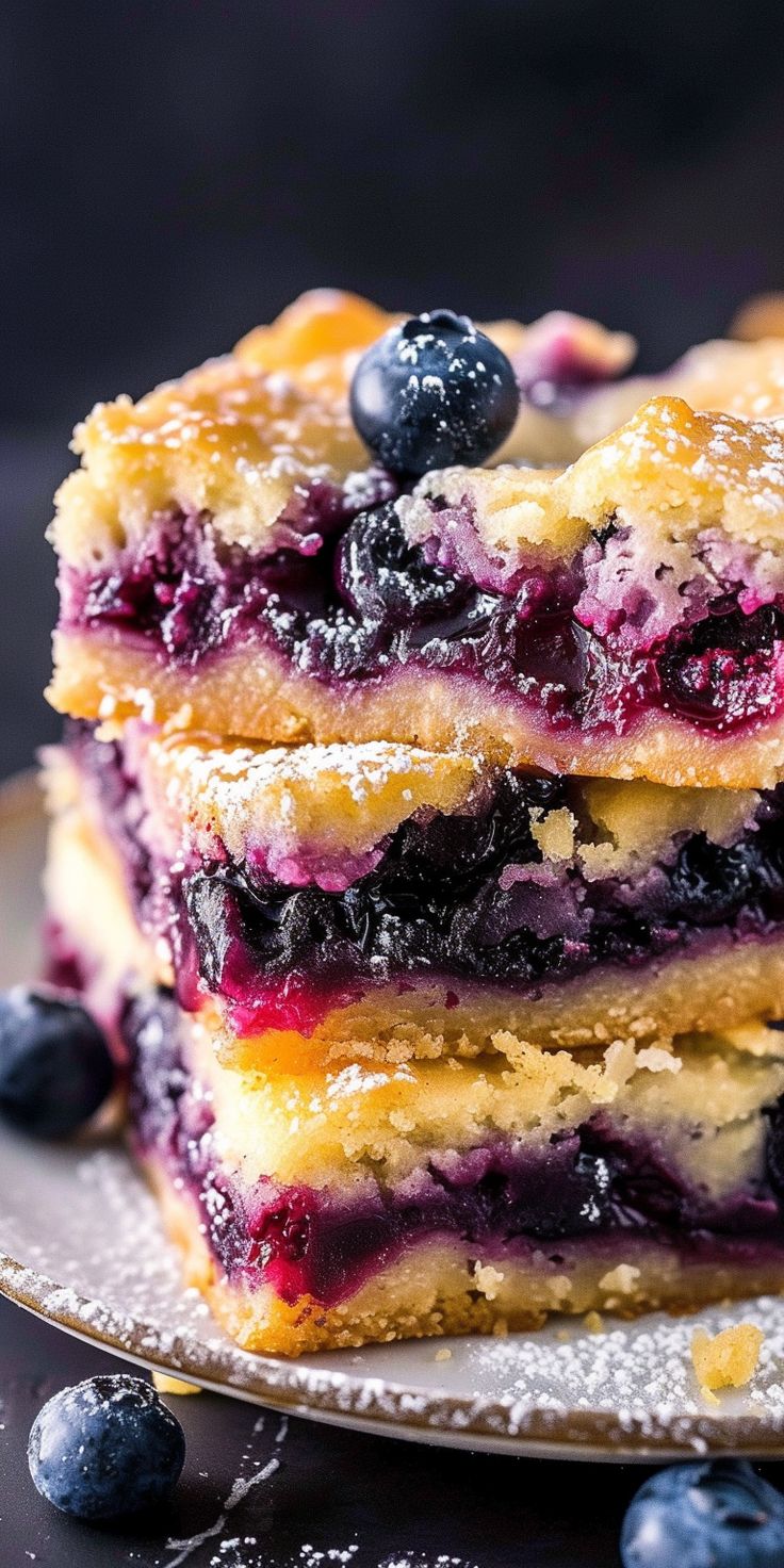 blueberry bars stacked on top of each other with powdered sugar and fresh berries