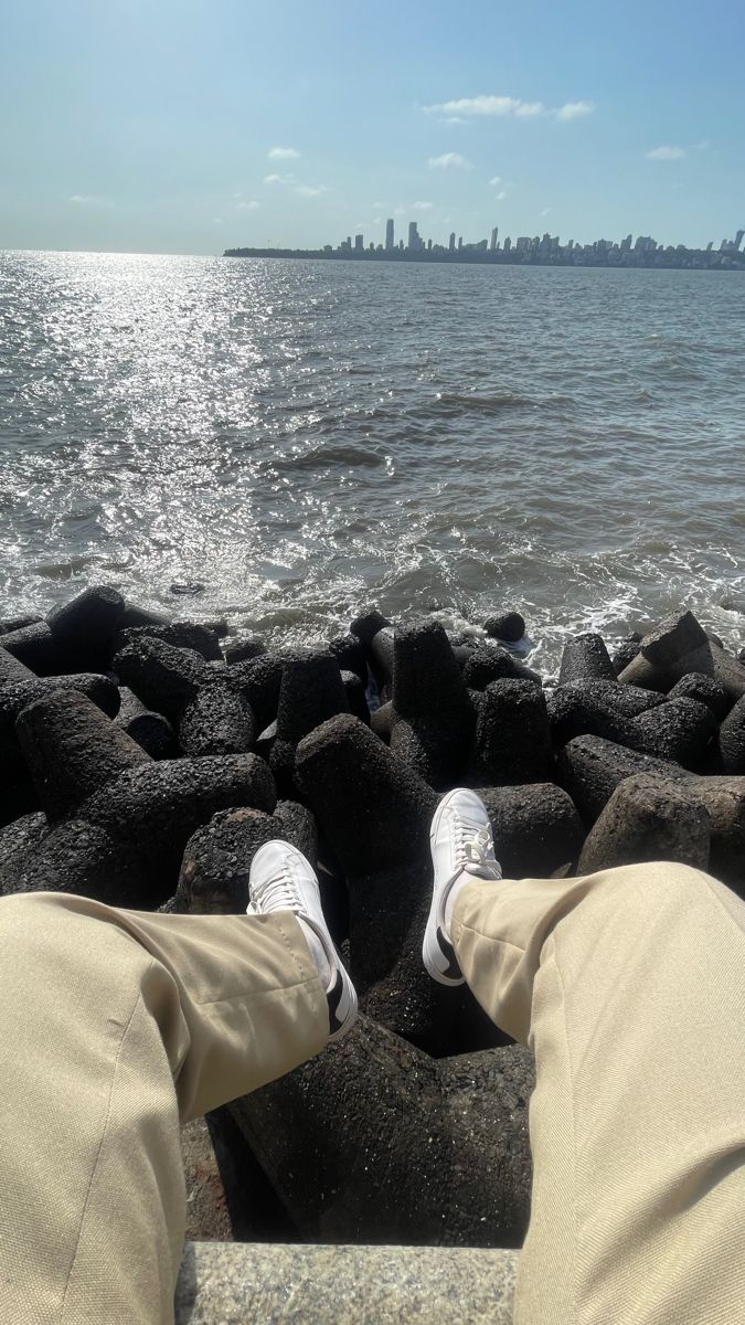 someone's feet on the edge of rocks by the water with a city in the background