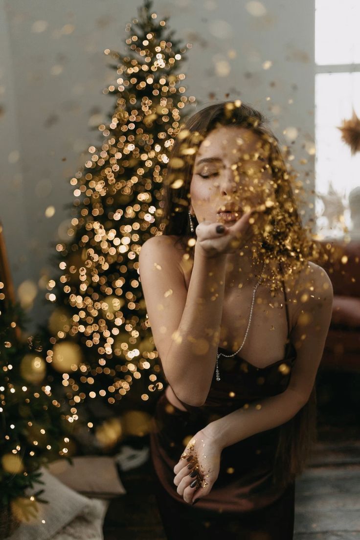 a woman standing in front of a christmas tree with her hand on her chin and looking at the camera