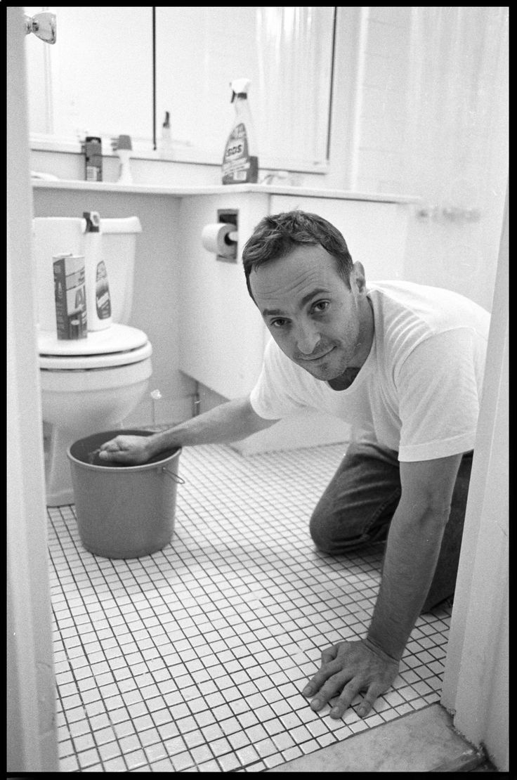 a man kneeling down on the floor in front of a toilet and trash can,