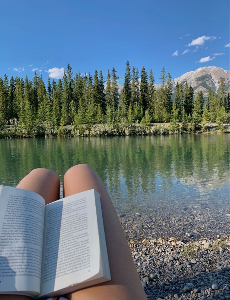 a person is reading a book on the shore of a lake