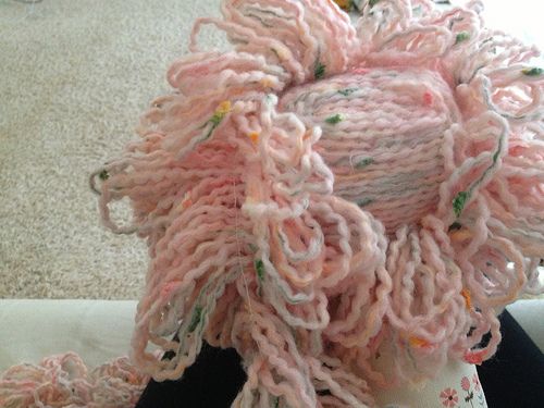 a knitted object sitting on top of a white vase with pink yarn around it