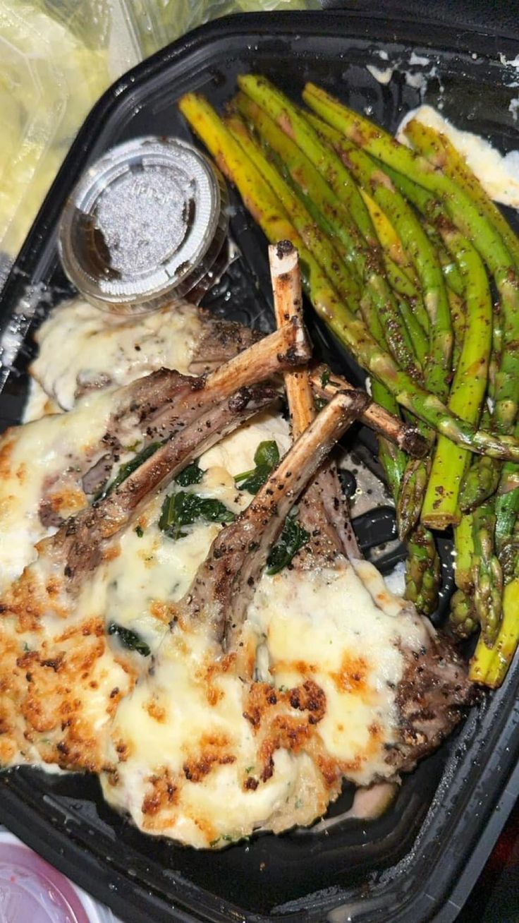 a plastic container filled with meat and asparagus on top of a bed of cheese