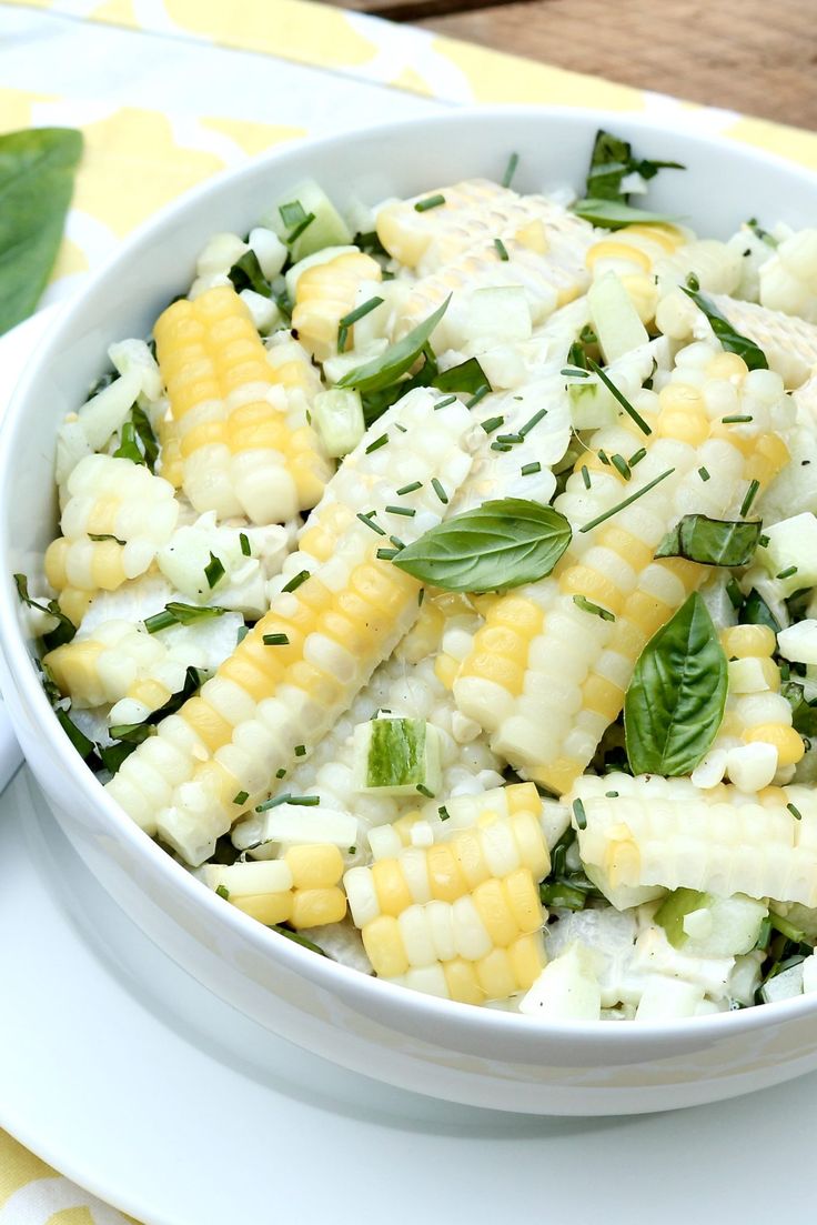 a white bowl filled with corn salad on top of a yellow and white table cloth