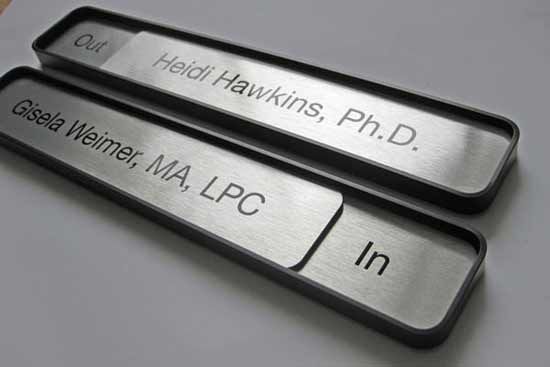 two black and silver metal name tags on a white surface with the names of three different companies