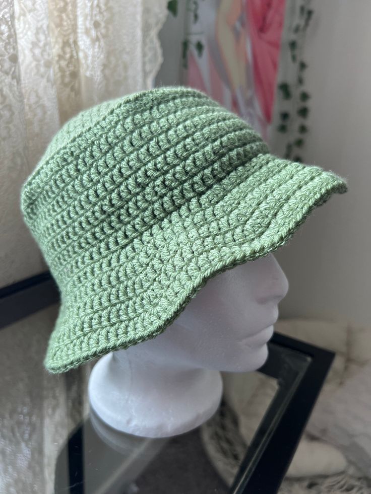 a white mannequin head wearing a green crocheted hat on top of a table