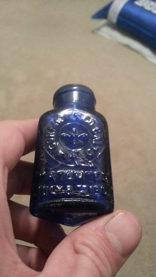 a hand holding a blue glass bottle with a skull design on the top and bottom