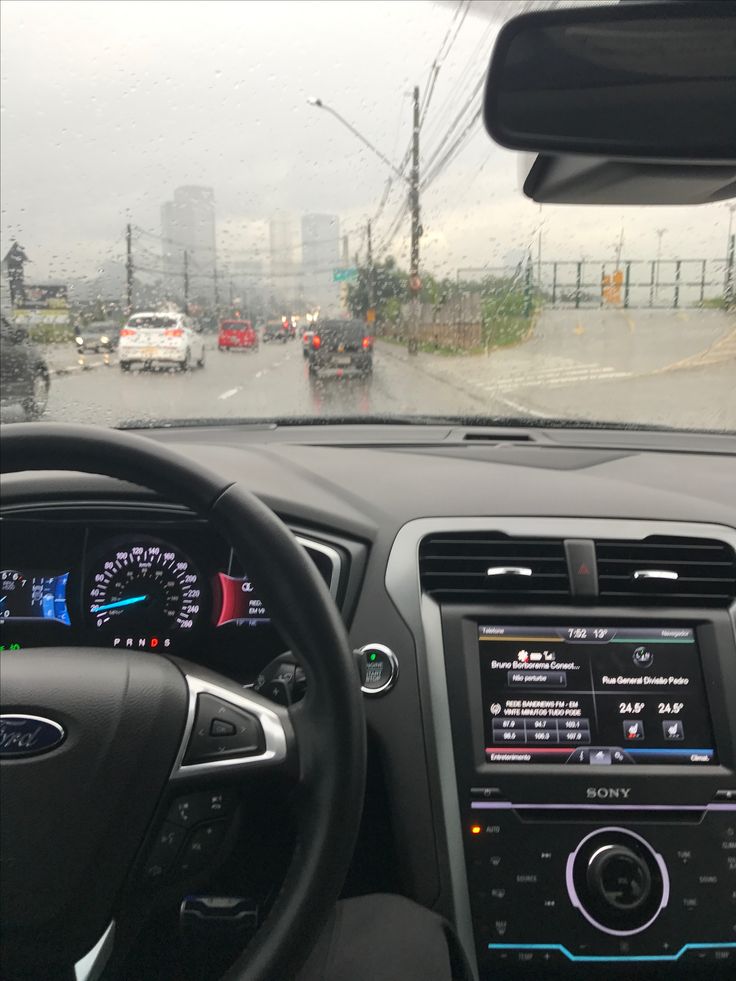 the dashboard of a car on a rainy day with cars driving down the road behind it