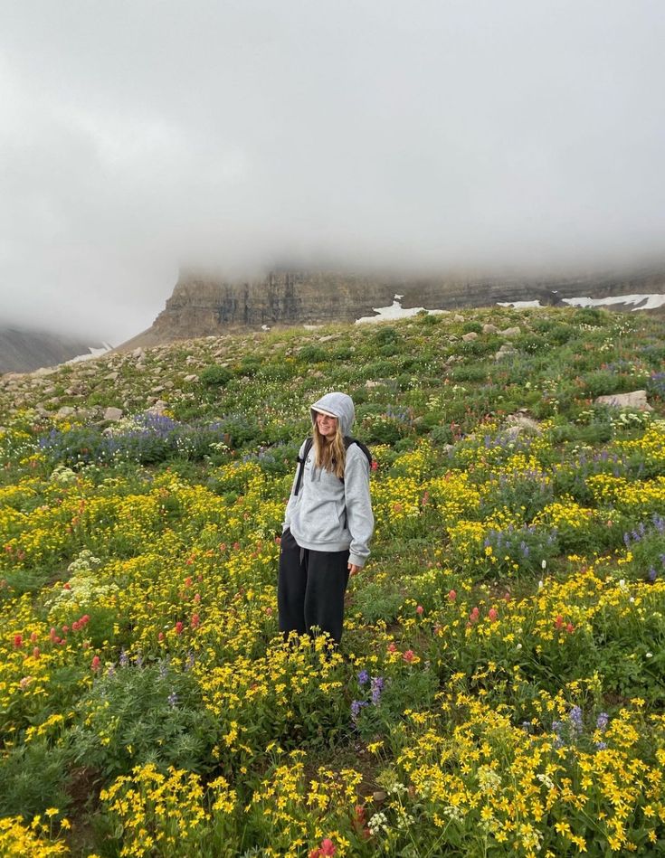 a woman standing on top of a lush green hillside covered in wildflowers and clouds