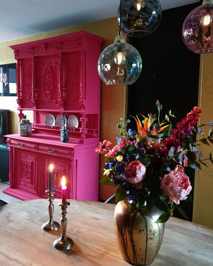 a vase filled with flowers sitting on top of a wooden table next to a pink cabinet