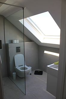 a white toilet sitting under a skylight in a bathroom next to a sink and window