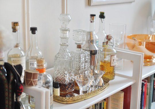 a shelf filled with liquor bottles and glasses on top of a white bookcase next to a wall