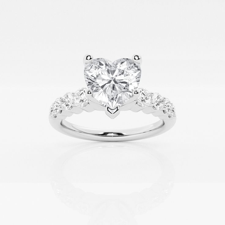 a heart shaped diamond ring with diamonds on the band and side stones set in 18k white gold