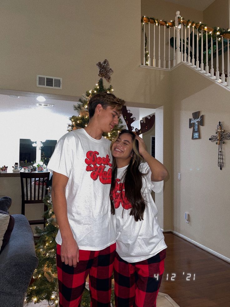 a man and woman standing in front of a christmas tree wearing matching pajama pants