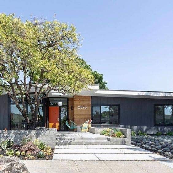 a modern house with trees and rocks in the front yard