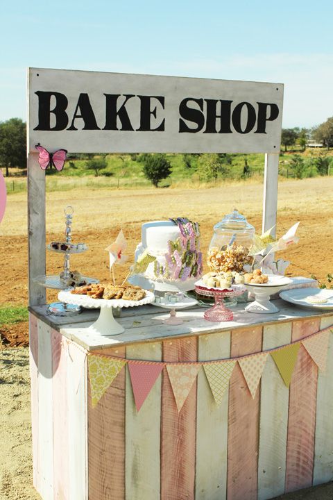 a cake shop stand is set up in the middle of a field with bunting and flags