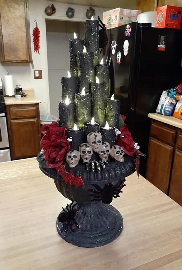 a table topped with candles and skulls on top of a vase filled with roses in front of a refrigerator