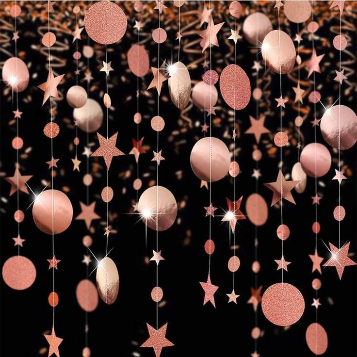 pink stars and balls hanging from strings on a black background with gold confetti