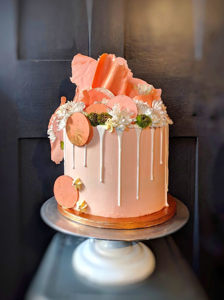 a pink and white cake with flowers on top sitting on a silver platter in front of a black wall