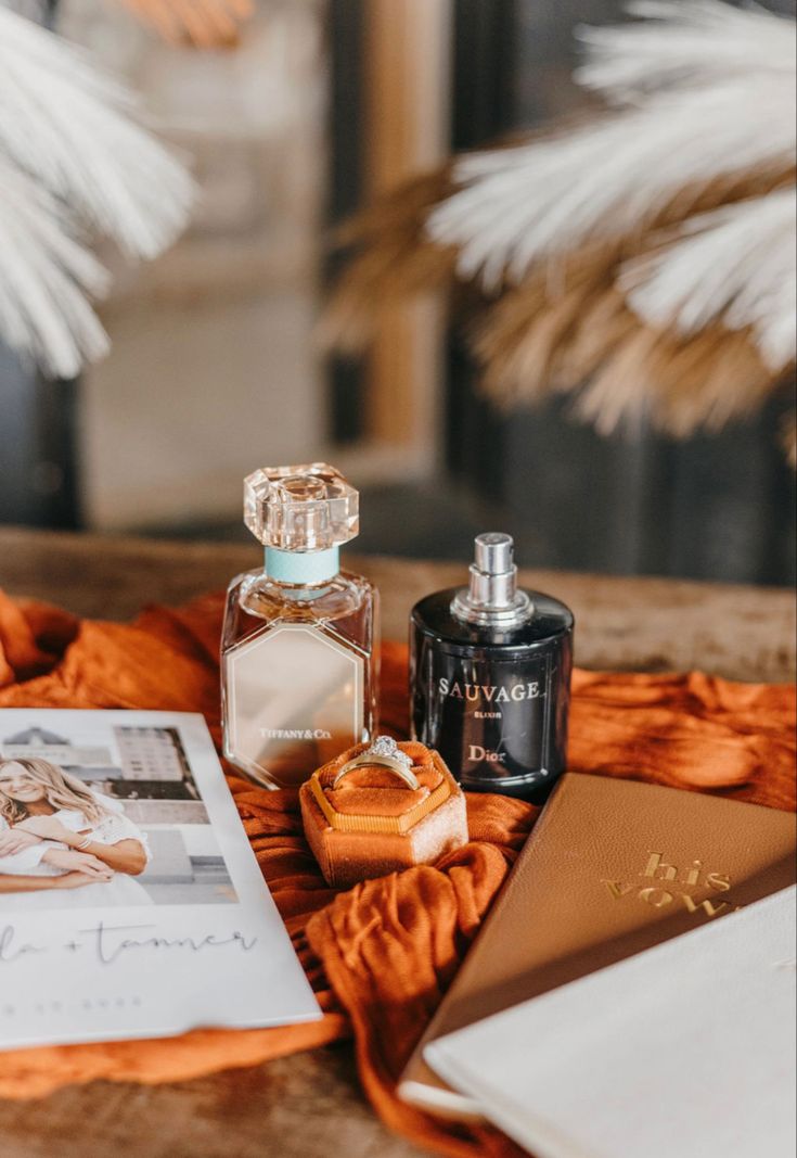 an open book, perfume bottle and other items on top of a table with feathers