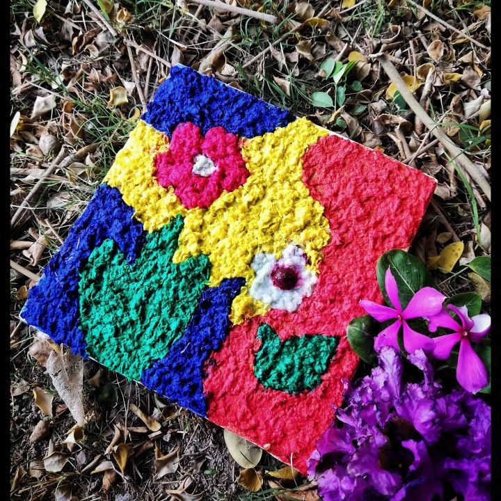 a colorful piece of art sitting on the ground next to flowers