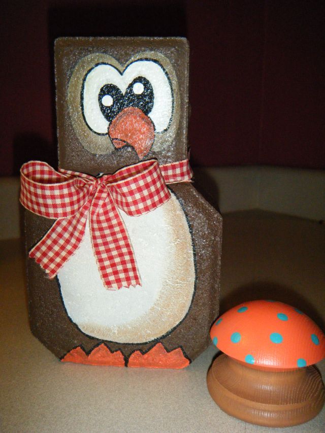 a penguin with a bow on its head sitting next to a toy mushroom and box