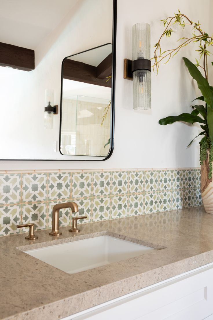 a bathroom sink sitting under a mirror next to a vase filled with green plants on top of a counter