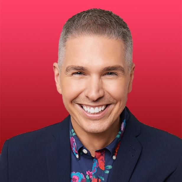 a man in a suit smiling at the camera with a red background behind him,